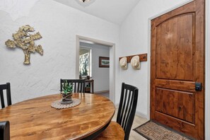 Een eetgedeelte met een houten tafel, stoelen, een decoratieve boom en een houten deur.