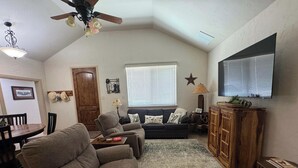 A living room with a ceiling fan, a television, a sofa, a coffee table, and a wooden cabinet. - 4-BD/2-BA Southern Retreat with Waterfront Patio (Gainesville)