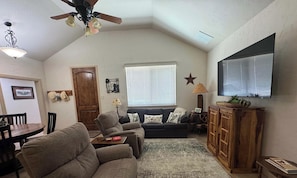 A living room with a ceiling fan, a television, a sofa, a coffee table, and a wooden cabinet. - 4-BD/2-BA Southern Retreat with Waterfront Patio (Gainesville)