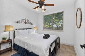 A bedroom with a bed, two bedside lamps, a ceiling fan, a window with blinds, and a decorative wall piece. - 4-BD/2-BA Southern Retreat with Waterfront Patio (Gainesville)