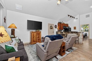 Een woonkamer met een bank, fauteuils, een televisie en een keuken met een eettafel.