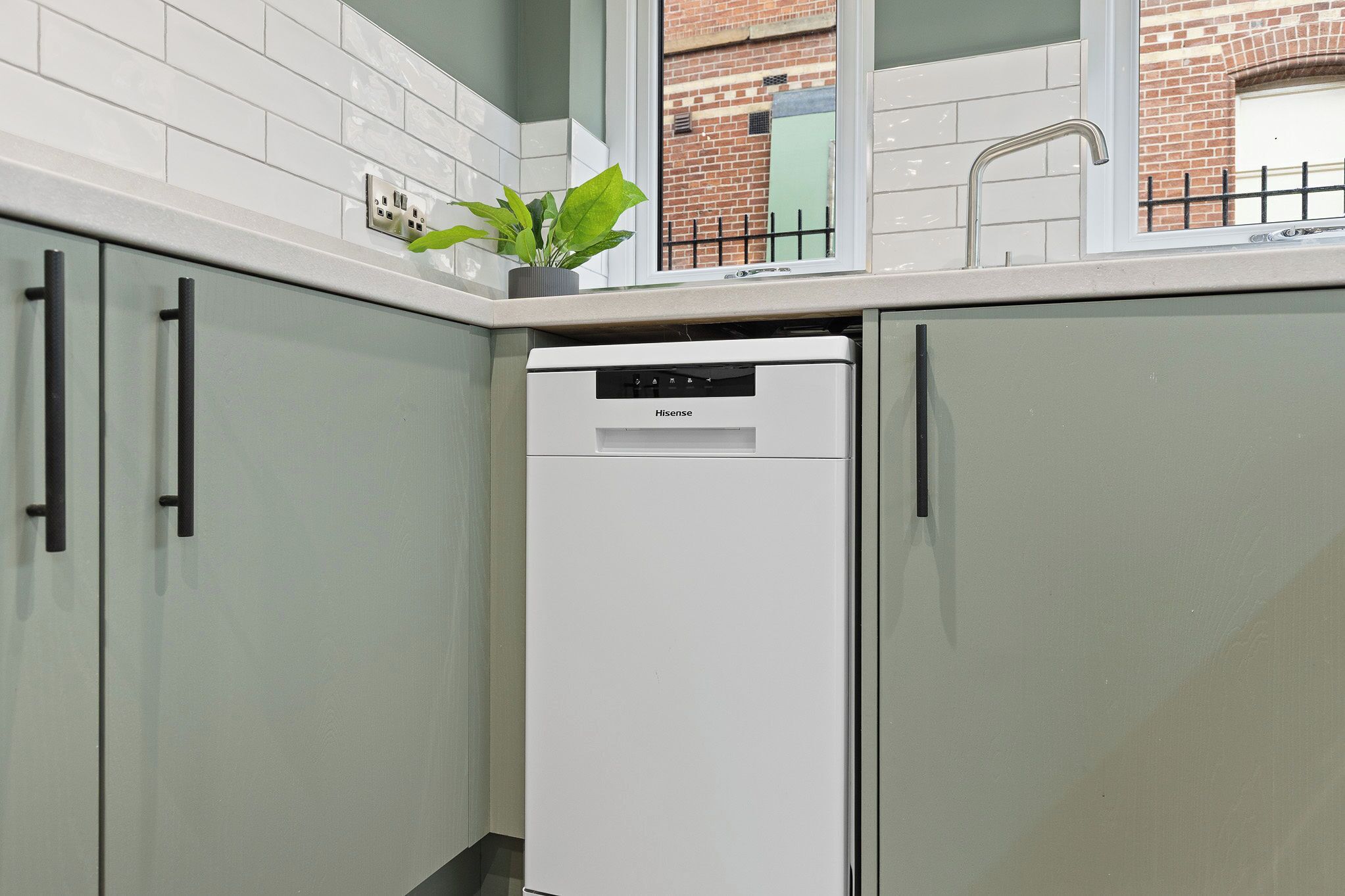 A compact kitchen with a white dishwasher, light-colored cabinets, and a small potted plant on the countertop.