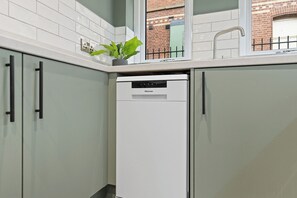 A compact kitchen with a white dishwasher, light-colored cabinets, and a small potted plant on the countertop. - 1 BED @ Victoria Court • Stay Angels (Sheffield)