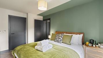 A hotel room with a bed, a bedside table, a lamp, and a green wall.