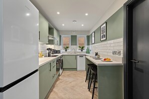 A modern kitchen with a dishwasher, sink, and bar stools. - 1 BED @ Victoria Court • Stay Angels (Sheffield)