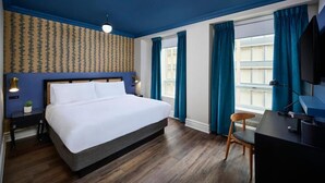 A hotel room with a large bed, a desk, a chair, a TV, and a window with curtains. - Classic Yonge Stay (Toronto)