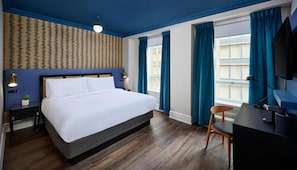 A hotel room with a large bed, a desk, a chair, a TV, and a window with curtains. - Classic Yonge Stay (Toronto)