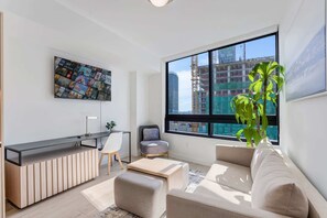A modern living room with a large window, a flat-screen TV, a sofa, a desk, and a potted plant. - Luxury Miami 1BR Apt, Pool & Beach Access for 4 (Miami)