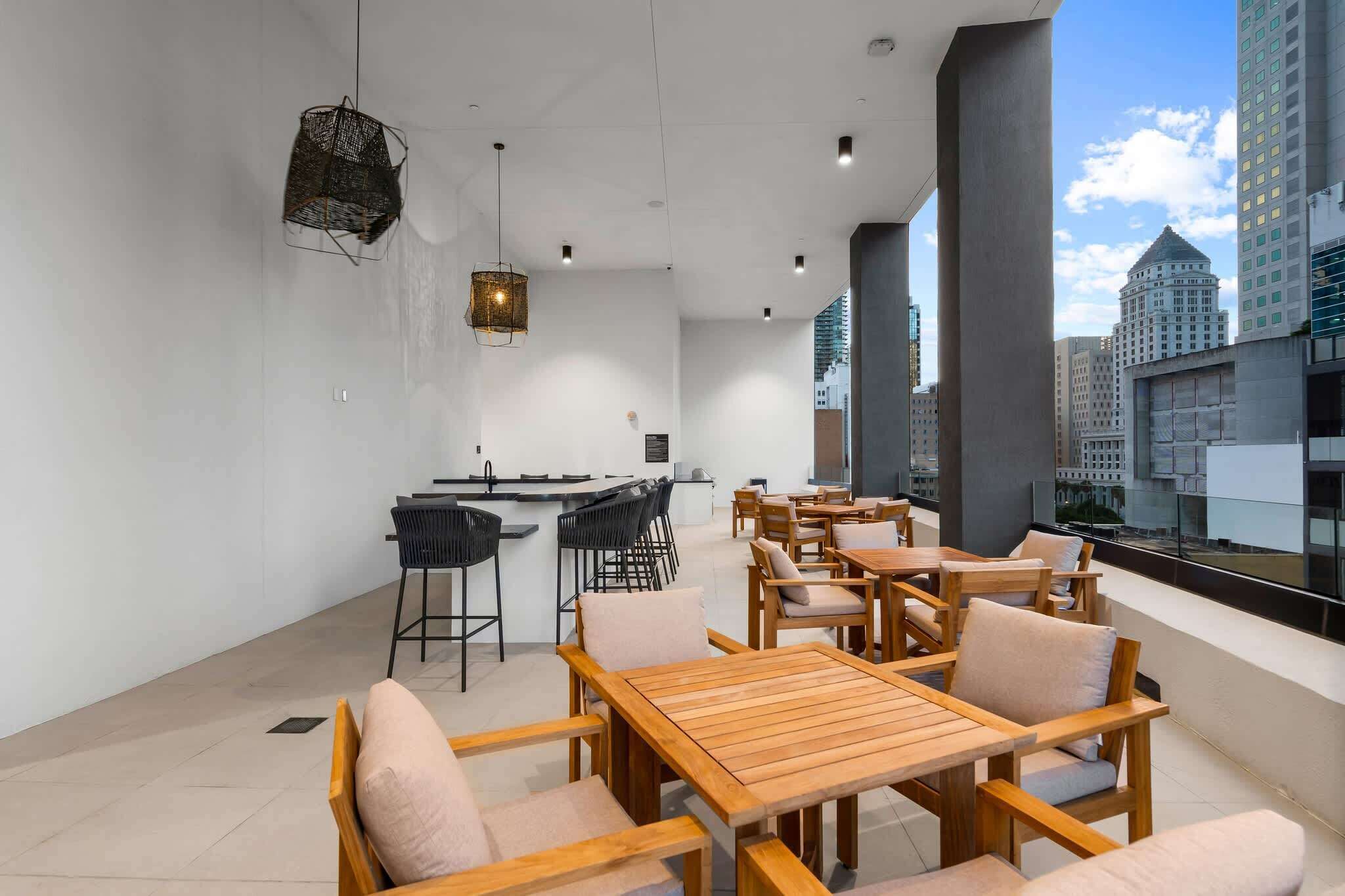 A modern interior with a bar area, seating, and large windows offering city views.