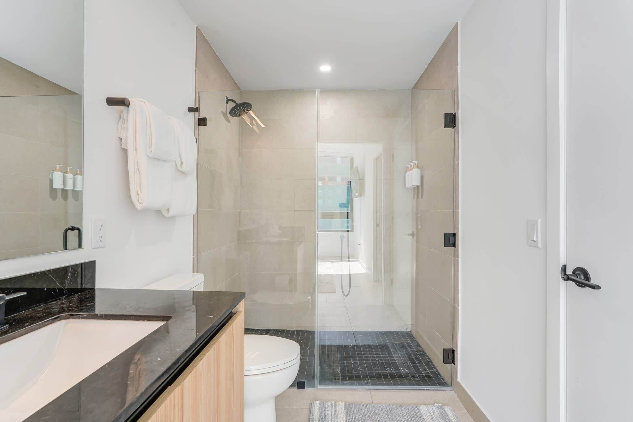 A modern bathroom with a glass-enclosed shower, a sink with a black countertop, and a toilet.