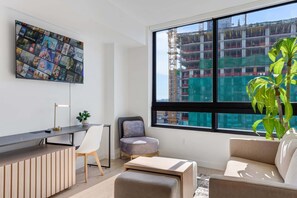 A modern living room with a large window, a mounted TV, a desk, and a plant. - Luxury Miami 1BR Apt, Pool & Beach Access for 4 (Miami)