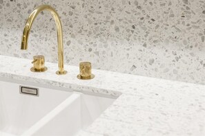 Ein Küchenspüle mit einem goldenen Wasserhahn, einer weißen Arbeitsplatte und einer Terrazzo-Spritzschutzwand.