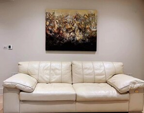 Ein beiges Ledersofa mit Kissen, ein an der Wand befestigtes abstraktes Gemälde und ein Thermostat.
