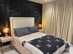 Ein modernes Schlafzimmer mit einem karrierten Kopfteil, einem Bett mit einer schwarz-weißen Decke, zwei Nachttischlampen und einem geometrischen Wanddesign.