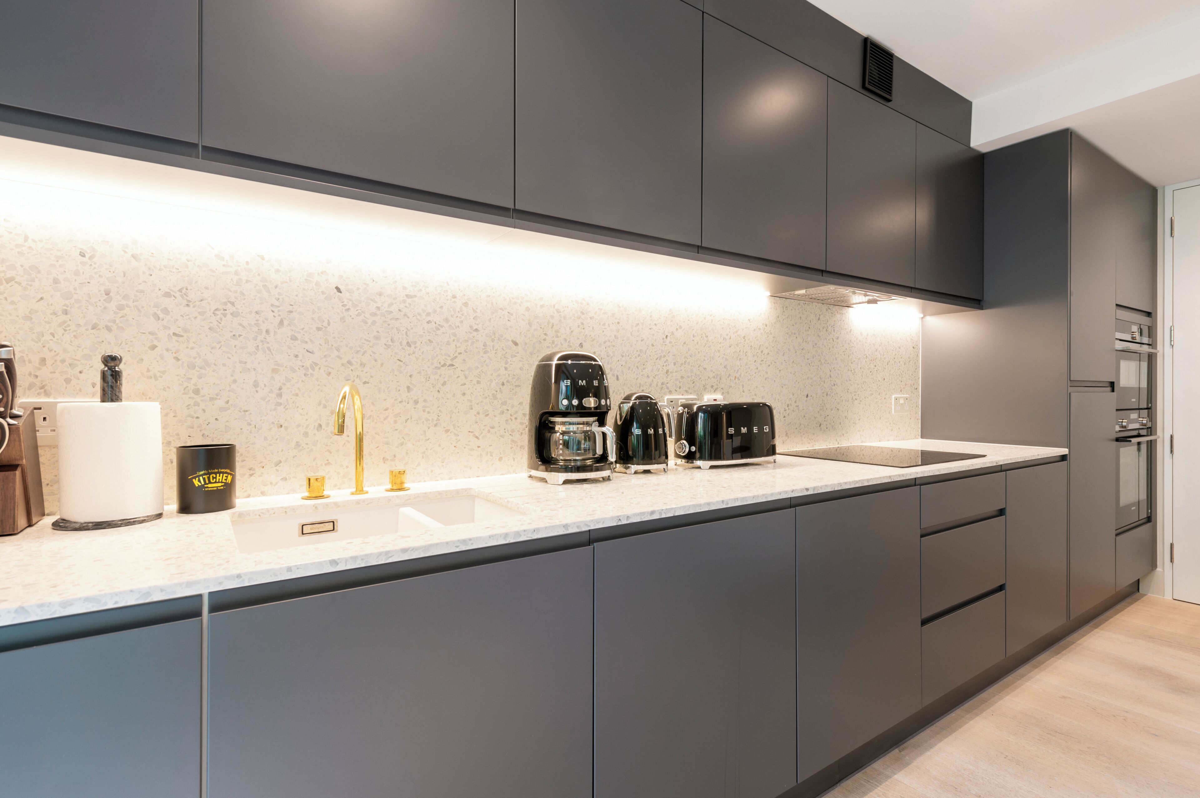A modern kitchen with grey cabinets, a white countertop, and a built-in oven.