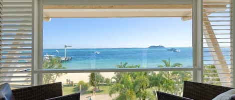 Un balcón con mobiliario de mimbre, vista al mar y un crucero en la distancia.