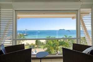 Un balcon agrémenté de meubles en osier, une vue sur la mer et un navire de croisière visible au loin.