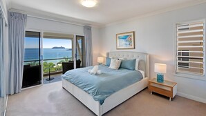Une chambre d’hôtel avec un grand lit, une vue sur la mer, un tableau au mur et une table de chevet avec une lampe.