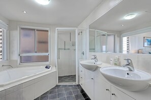 Un baño moderno con bañera, dos lavamanos, cabina de ducha de vidrio y un espejo grande.