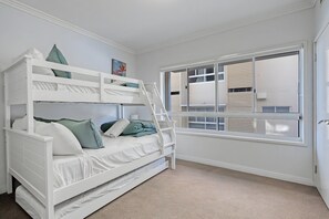 Ein Stockbett mit einer Leiter, ein Fenster mit Jalousien und ein Teppichboden.
