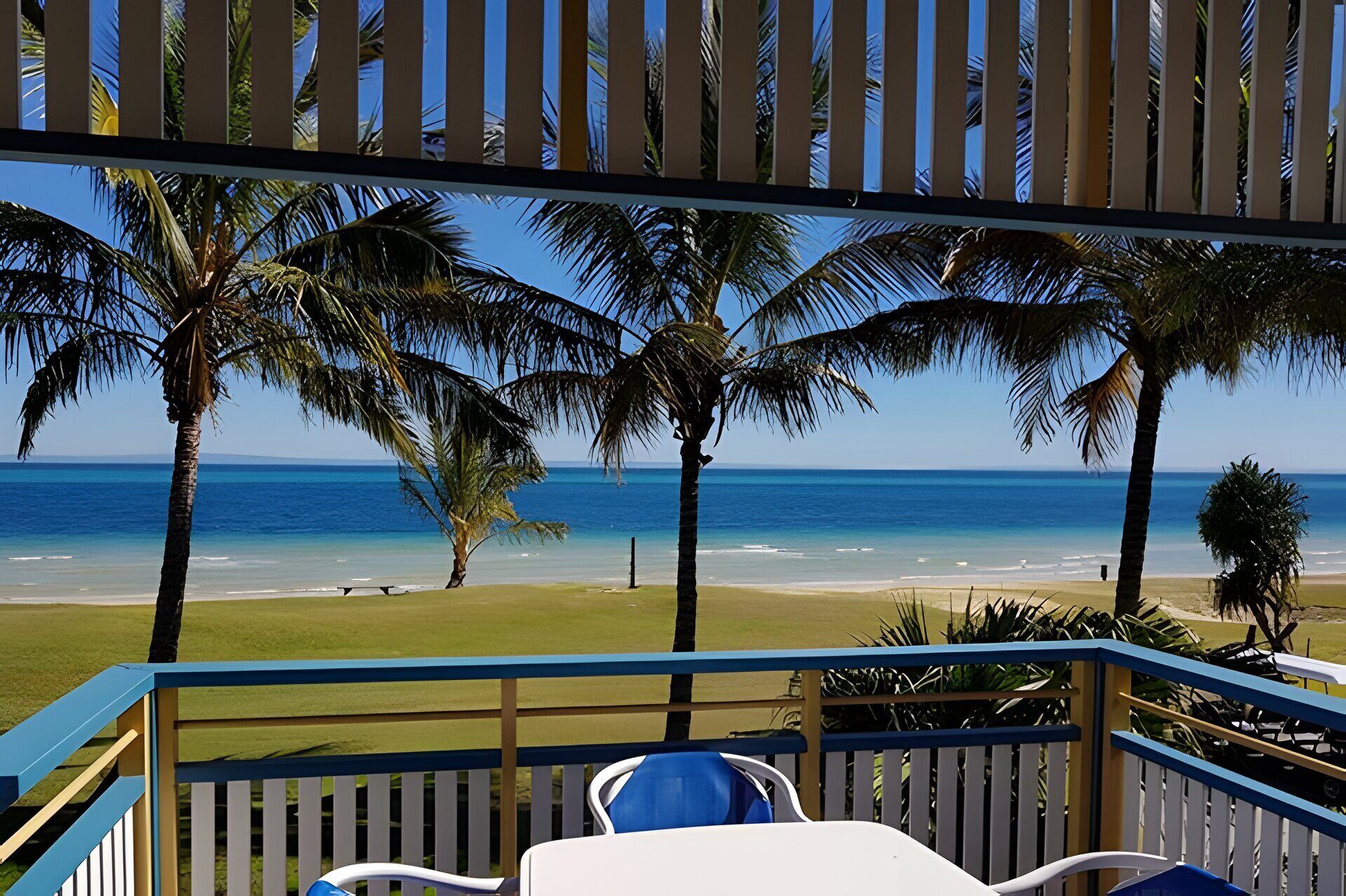 Vista sulla spiaggia da un balcone coperto, con palme e cielo sereno.