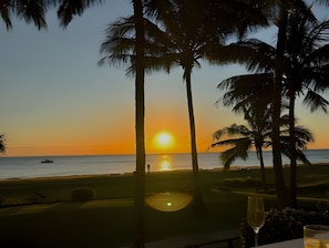 Sonnenuntergangsblick von einer Strandlage mit Palmen und einem Tisch mit einem Glas.