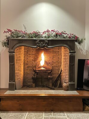 A fireplace with a fire, a decorative mantel, and a television on the right. - Unique London family-sized home with stunning Natural Pool (London)