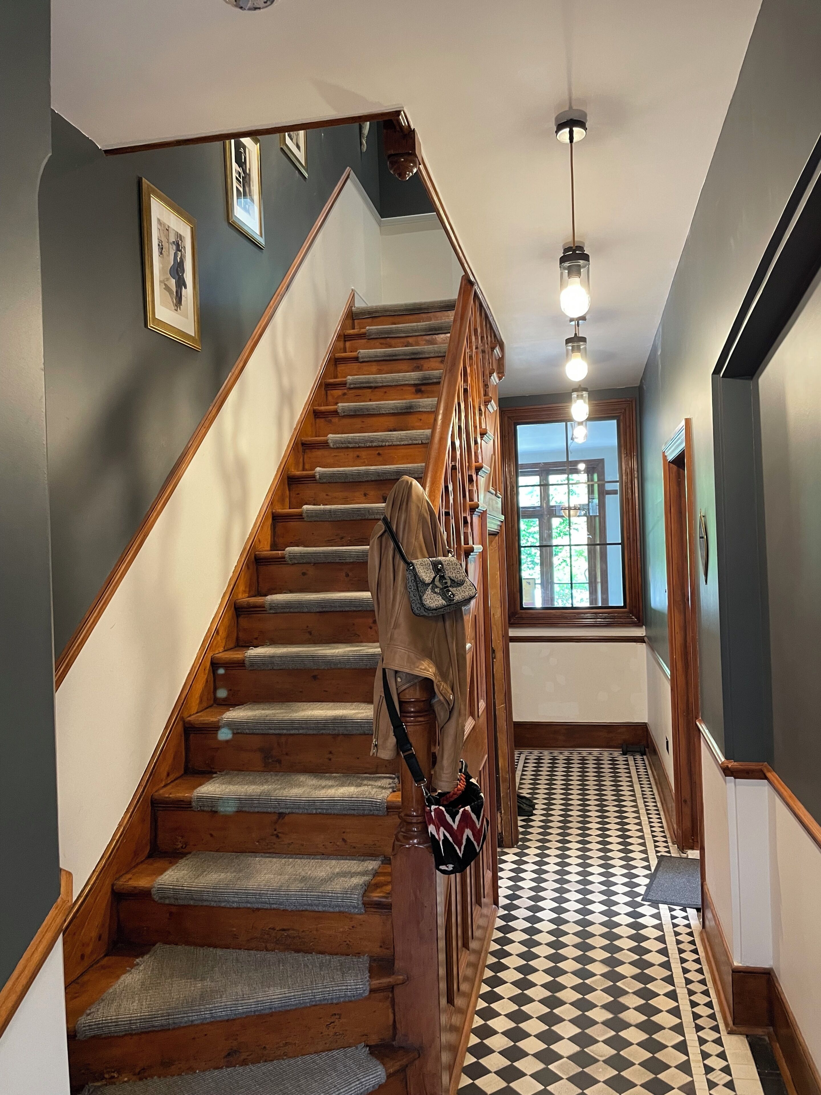 A wooden staircase with a patterned floor, a hanging bag, and a door leading to a room with a window.
