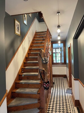 A wooden staircase with a patterned floor, a hanging bag, and a door leading to a room with a window. - Unique London family-sized home with stunning Natural Pool (London)