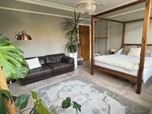 A bedroom with a four-poster bed, a leather sofa, a large potted plant, and a patterned rug. - Unique London family-sized home with stunning Natural Pool (London)