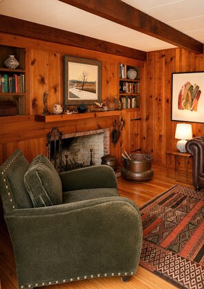 A cozy living room with a fireplace, a green armchair, a wooden bookshelf, and a patterned rug. - Boutique Riverside Retreat (Seaford)