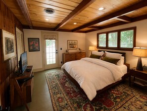 A bedroom with a large bed, a wooden desk, a television, and a window with a view of trees. - Boutique Riverside Retreat (Seaford)
