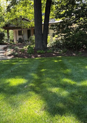 A well-maintained lawn with a gazebo, a house with a porch, and a large tree in the foreground. - Boutique Riverside Retreat (Seaford)