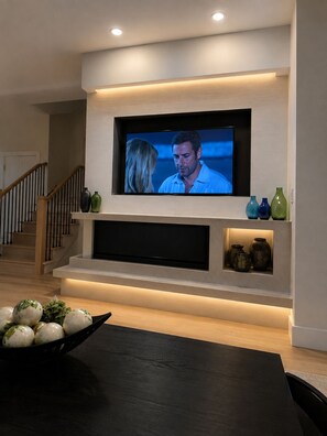 Una sala de estar moderna con un televisor de pantalla plana montado en la pared, una escalera y jarrones decorativos.