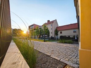 Ein gepflasterter Innenhof mit Gebäuden im Hintergrund, einem klaren Himmel und Sonnenschein.