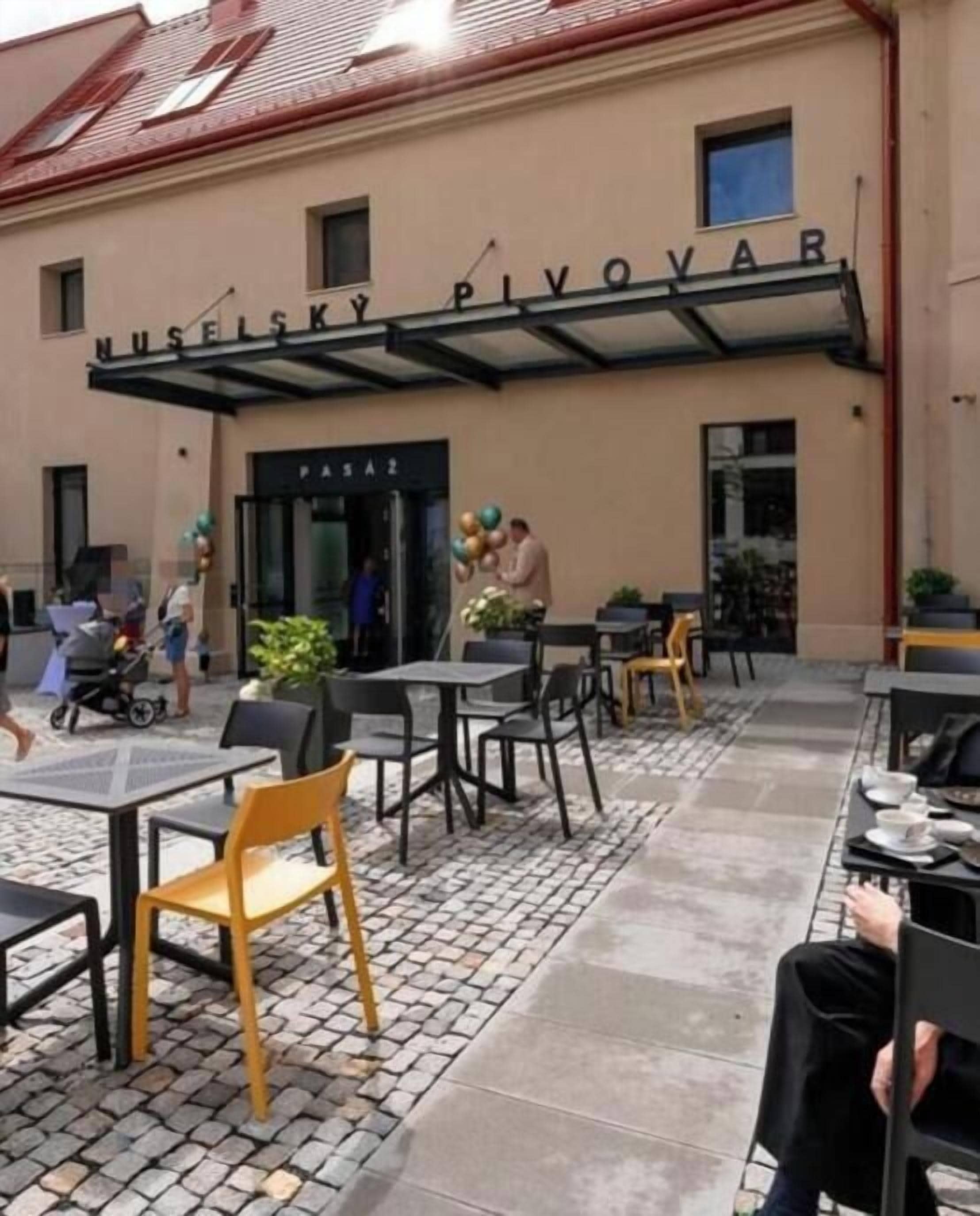 An outdoor seating area with tables and chairs, a covered entrance, and a building with signage.