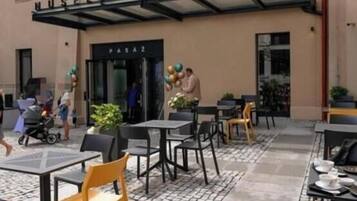 An outdoor seating area with tables and chairs, a covered entrance, and a building with signage.