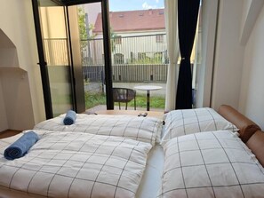 Ein Schlafzimmer mit zwei Betten, einem Balkon mit Tisch und Stühlen und Blick ins Freie.