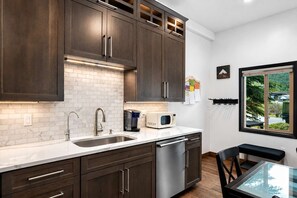 A modern kitchen with dark wood cabinets, a white marble countertop, stainless steel appliances, and a view of the outdoors through a window. - The Creekside Retreat | Steps to Frisco’s Main St! (Frisco)