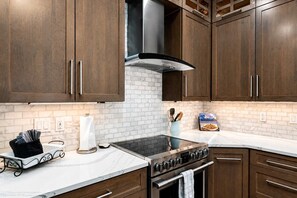 A kitchen with dark wooden cabinets, a stainless steel range hood, a white marble countertop, and a built-in oven. - Frisco Retreat | Creekside • Unbeatable Location (Frisco)