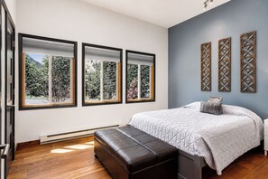 A bedroom with a bed, a bench, and three windows with a view of greenery. - Frisco Retreat | Creekside • Unbeatable Location (Frisco)