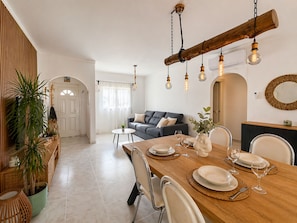 Een eetgedeelte met een houten tafel gedekt voor twee personen, een bank op de achtergrond en een hanglamp.