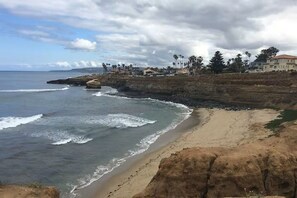 Eine Küstenlandschaft mit Sandstrand, Felsen und einer Reihe von Gebäuden mit Palmen.