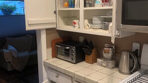 Une cuisine compacte avec des meubles blancs, un four à micro-ondes encastré, un grille-pain et une cuisinière.