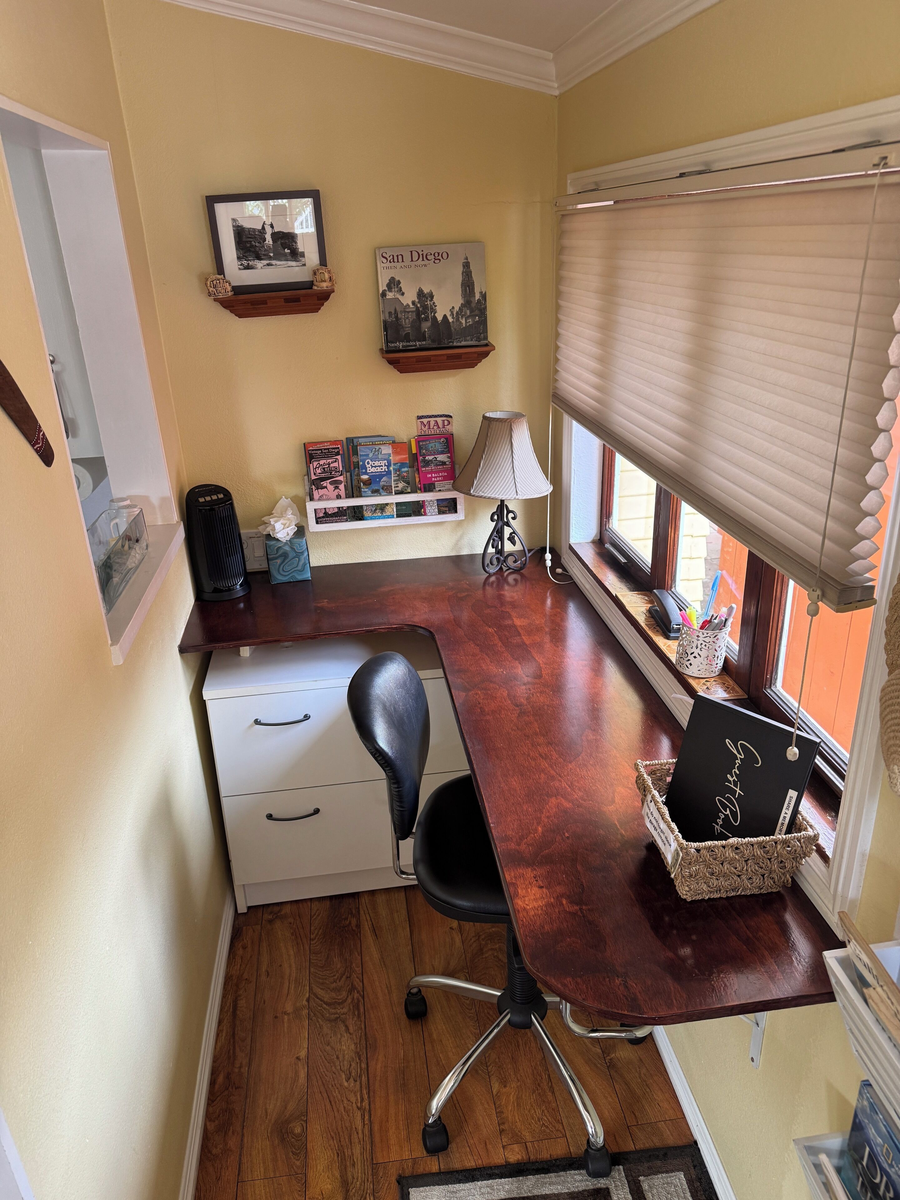 Ein Arbeitszimmer mit Schreibtisch, Stuhl, Büchern, einer Lampe und einem Fenster mit Jalousien.