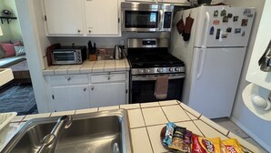 Une cuisine avec des meubles blancs, un four à micro-ondes, un four traditionnel, une cuisinière, un évier et un réfrigérateur décoré d’aimants.
