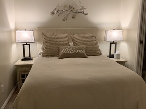 Ein ordentlich bezogenes Bett mit einem 'Welcome'-Kissen, zwei Nachttischlampen und einer Wandleuchte.