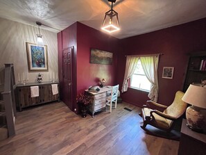 Ein Zimmer mit Holzboden, einem Schreibtisch mit Schreibmaschine, einem Stuhl, einem Bücherregal und einem fenster mit Vorhängen.
