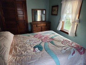 Quarto com cama, cómoda de madeira, espelho e janela com cortinas.