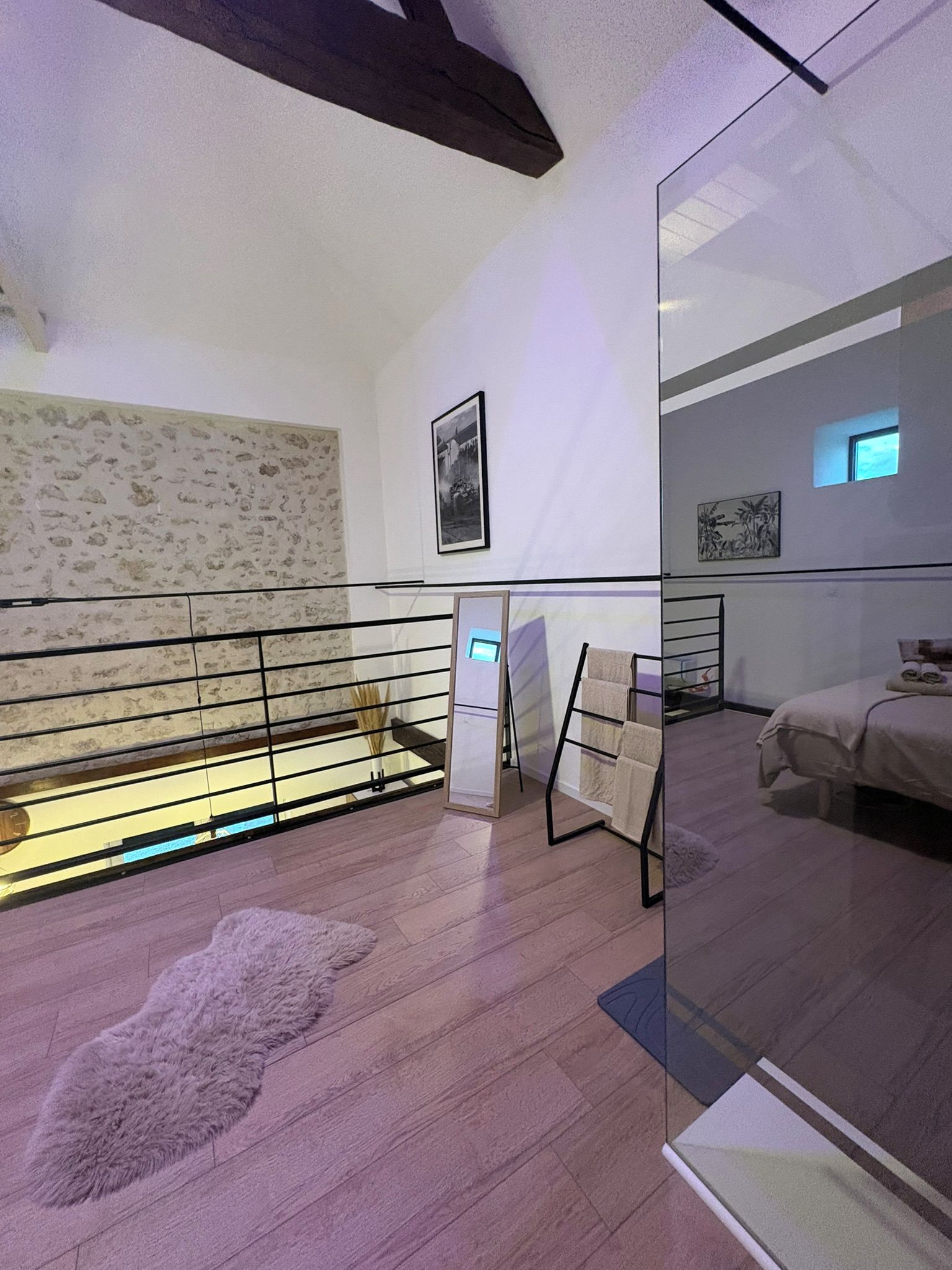 Un dormitorio moderno con suelo de madera, un separador de vidrio, una cama y un ventanal pequeño.